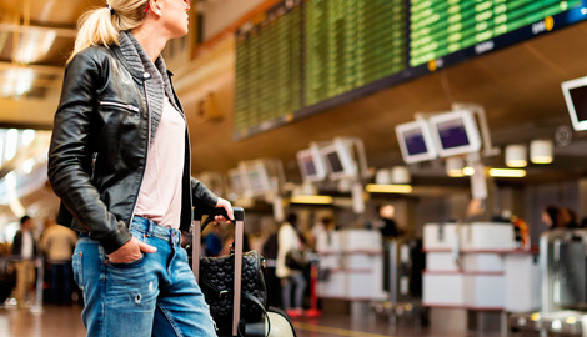 Frau mit Koffer schaut auf Monitor mit Abflugzeiten