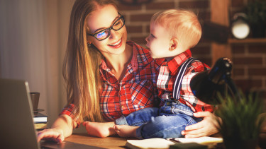 Mutter sitzt mit Baby vor Laptop